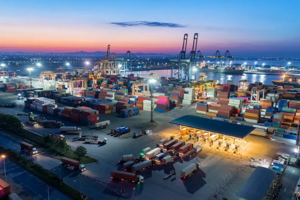 Large port with containers, cranes, and ships at dusk.